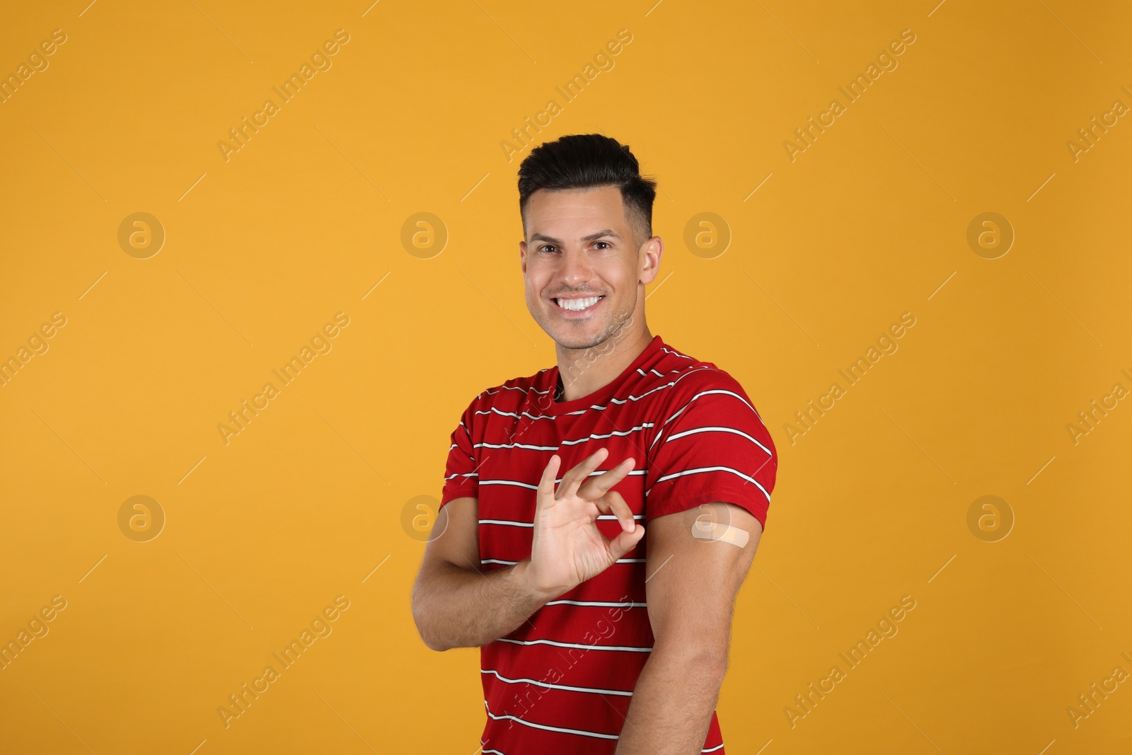 Photo of Vaccinated man with medical plaster on his arm showing okay gesture against yellow background