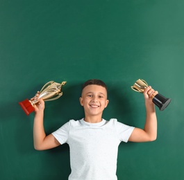 Happy boy with golden winning cups near chalkboard