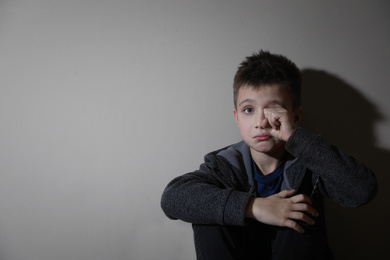 Crying little boy near beige wall, space for text. Domestic violence concept