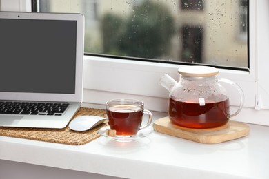 Photo of Modern laptop and tea on white sill near window