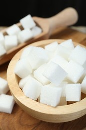 Photo of White sugar cubes in bowl and scoop on wooden board, closeup