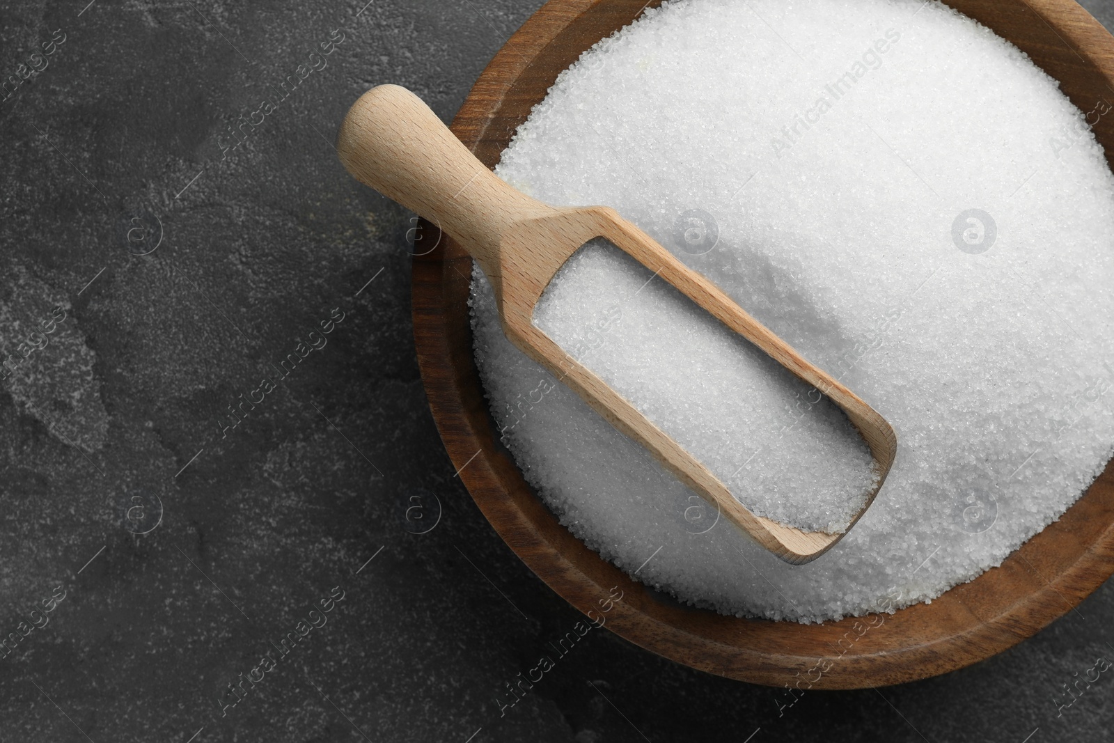 Photo of Granulated sugar in bowl and scoop on grey textured table, top view. Space for text