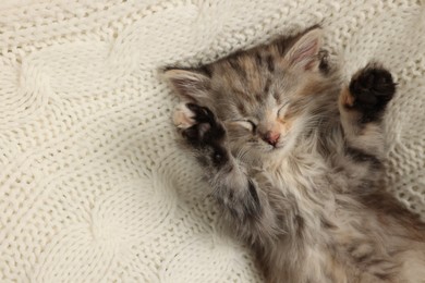 Cute kitten sleeping on white knitted blanket, top view. Space for text