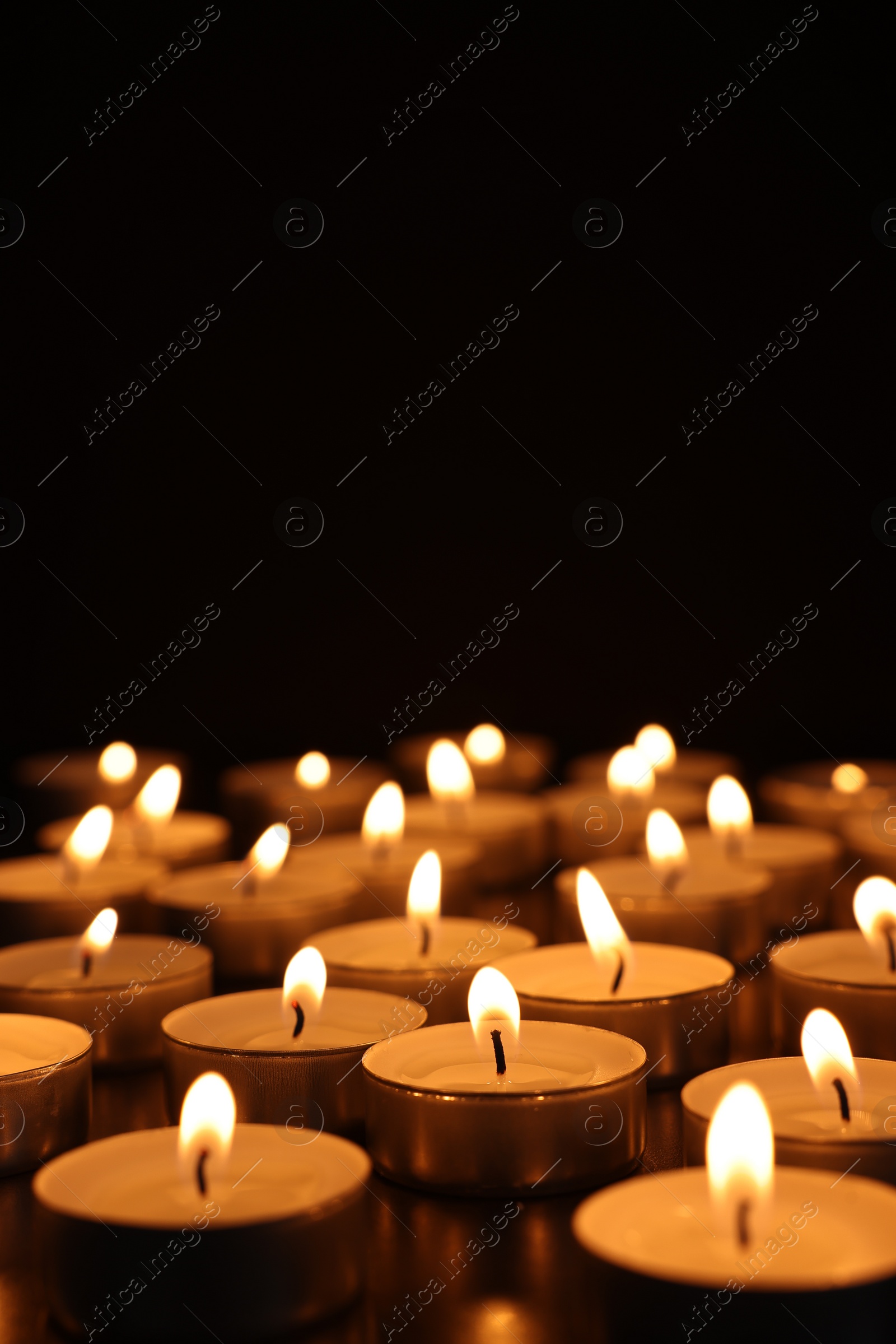 Photo of Burning candles on dark surface against black background, space for text