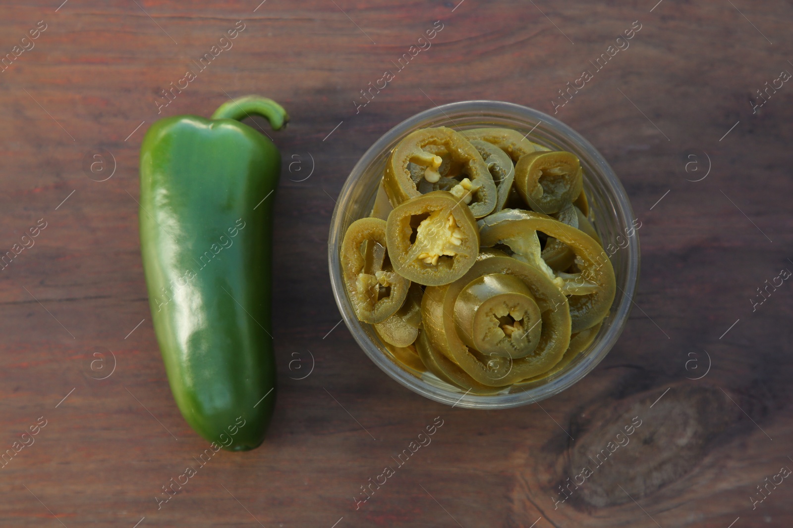 Photo of Fresh and pickled green jalapeno peppers on wooden table, flat lay