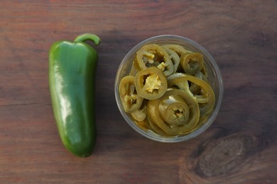 Photo of Fresh and pickled green jalapeno peppers on wooden table, flat lay