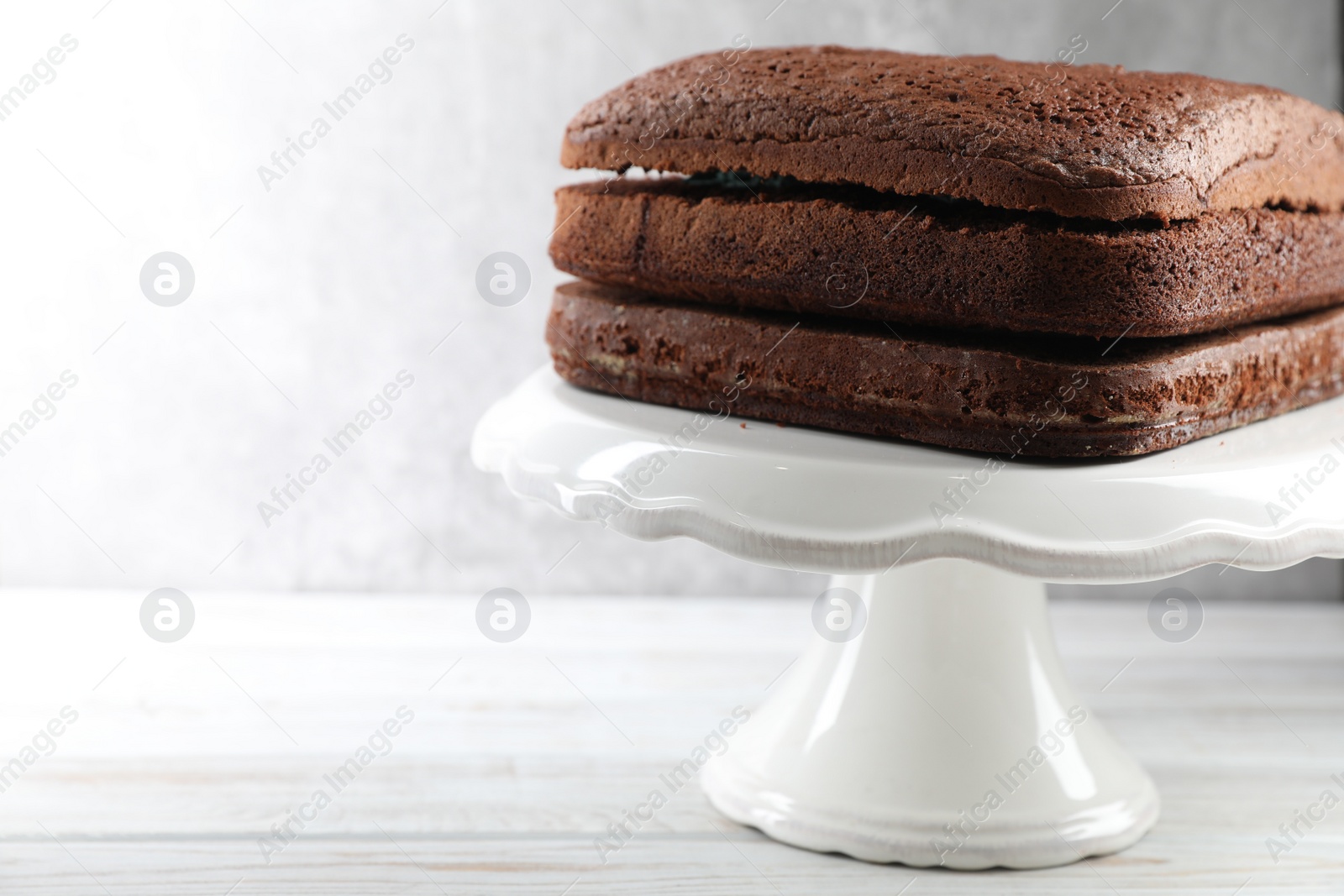 Photo of Stand with layers of homemade chocolate sponge cake on white wooden table, closeup. Space for text
