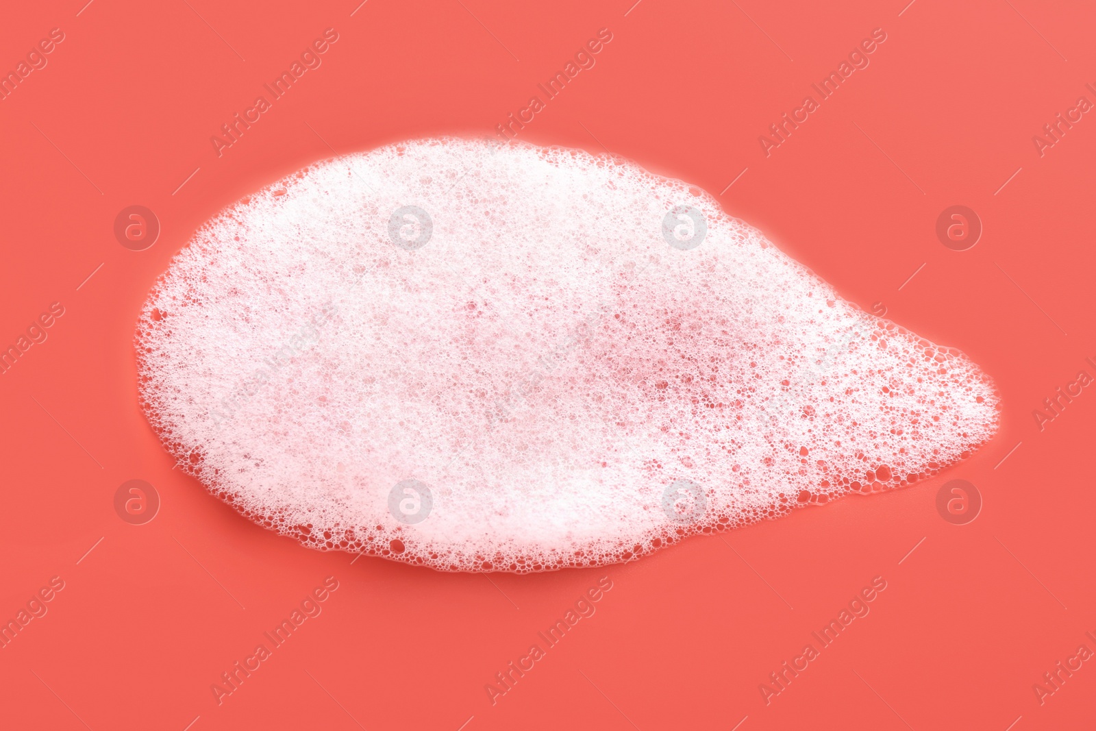 Photo of White foam with bubbles on coral background, top view