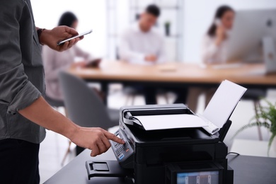 Photo of Employee using modern printer in office, closeup