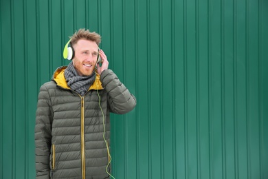 Young man listening to music with headphones against color wall. Space for text