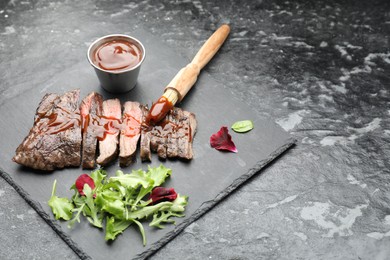 Photo of Pieces of delicious roasted beef meat with sauce and greens on black table. Space for text