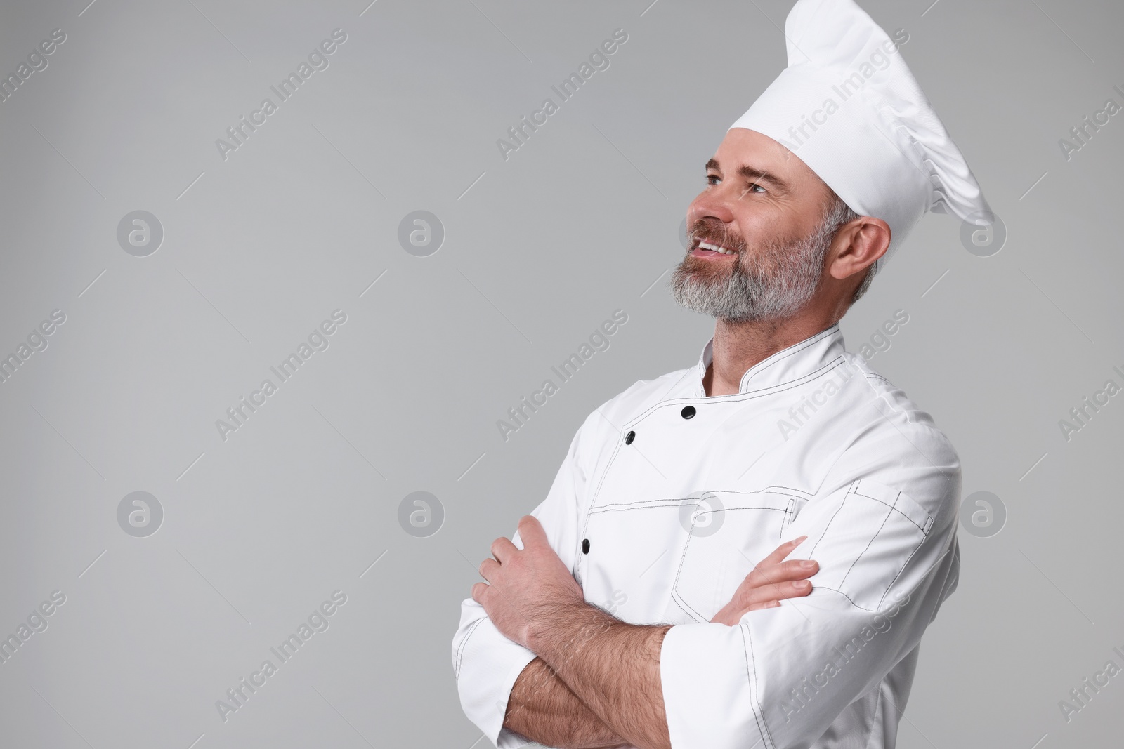 Photo of Happy chef in uniform on grey background, space for text