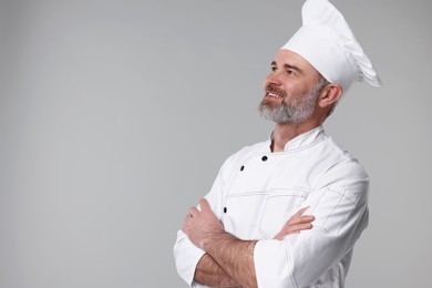 Happy chef in uniform on grey background, space for text