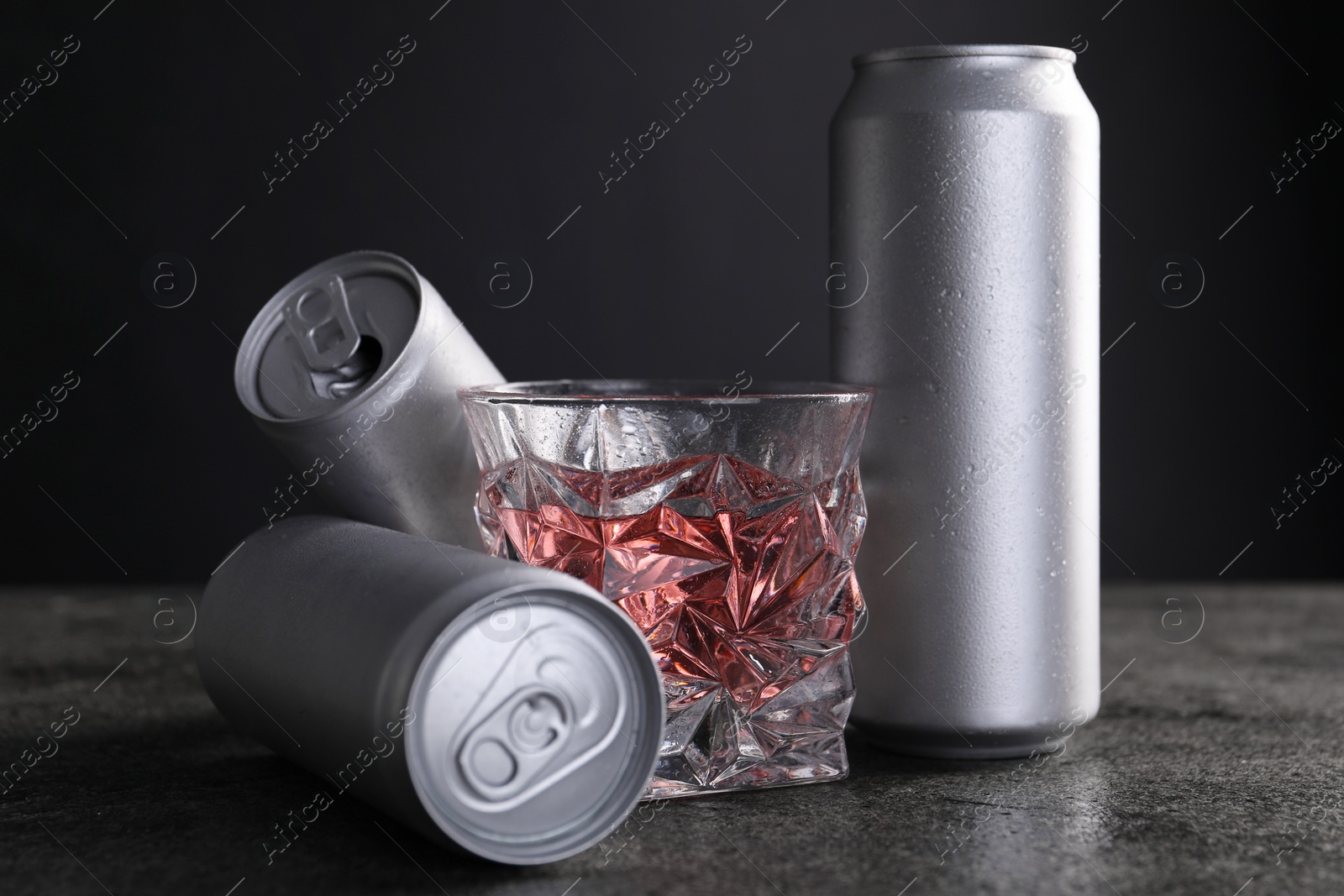 Photo of Energy drink in glass and aluminium cans on grey table, closeup