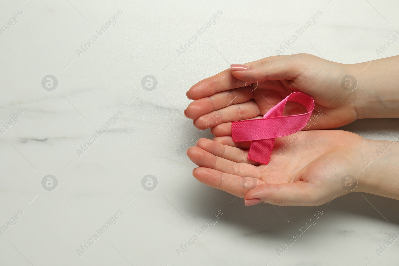 Photo of Breast cancer awareness. Woman with pink ribbon at white marble table, top view. Space for text