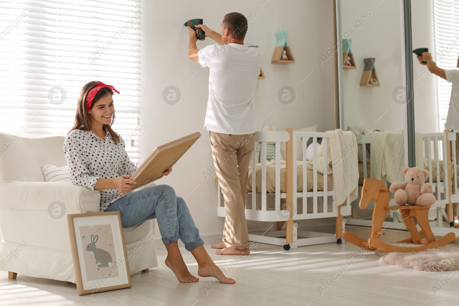 Photo of Happy couple decorating baby room with pictures together. Interior design