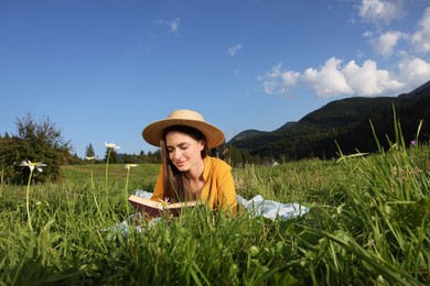 Beautiful young woman reading book on green meadow in mountains