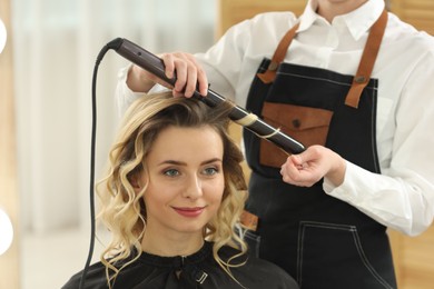 Hair styling. Hairdresser curling woman's hair in salon, closeup