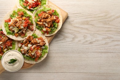 Photo of Delicious tacos with vegetables, meat and sauce on white wooden table, top view. Space for text