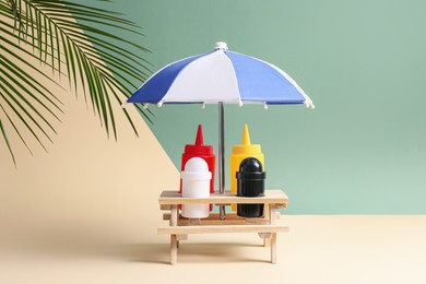 Photo of Wooden holder with different sauces, spices and toy umbrella on color background