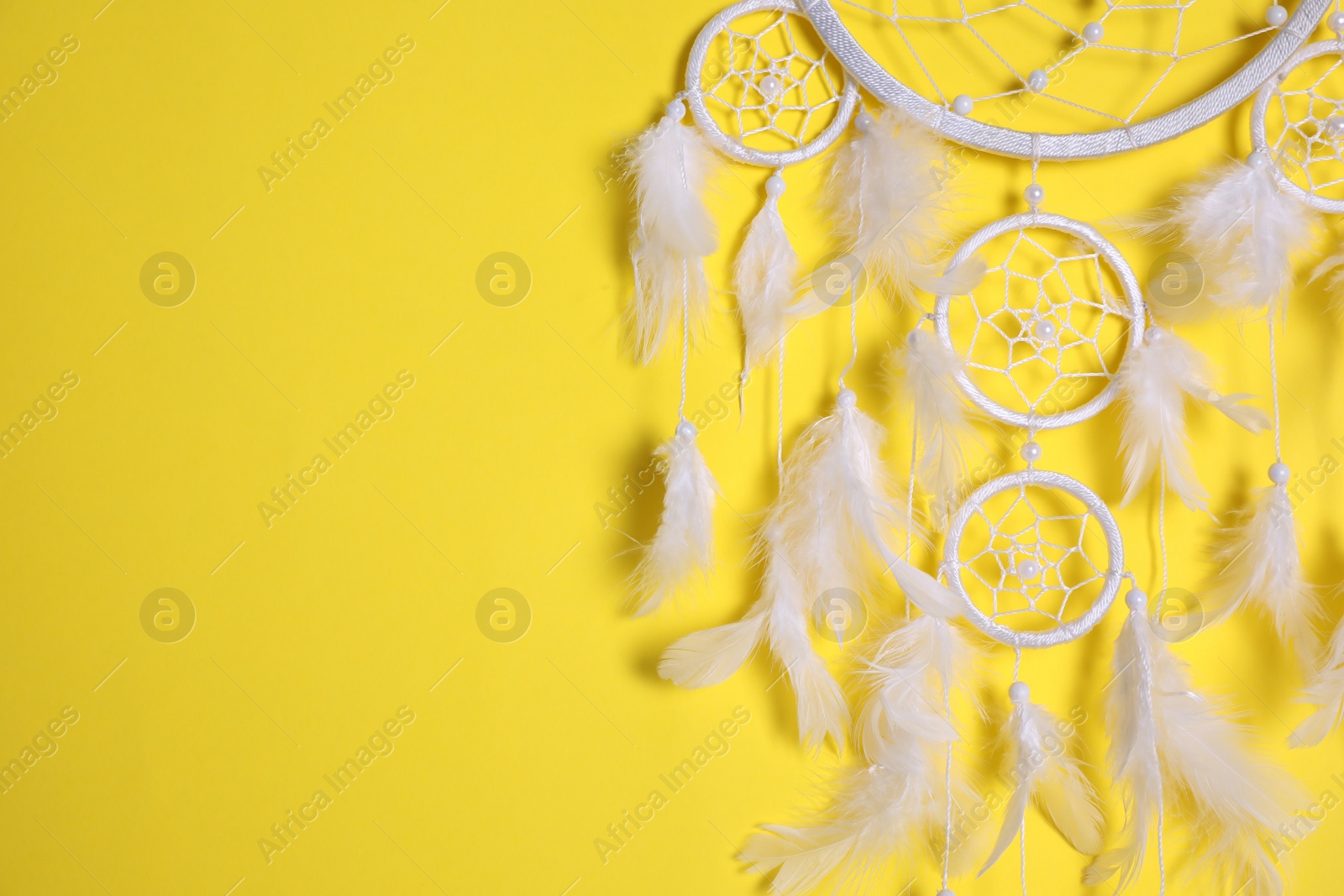 Photo of Beautiful dream catcher hanging on yellow background, closeup. Space for text