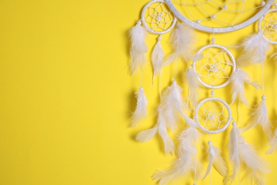 Beautiful dream catcher hanging on yellow background, closeup. Space for text