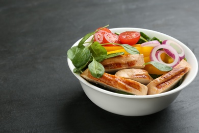 Photo of Delicious salad with chicken, vegetables and spinach on black table