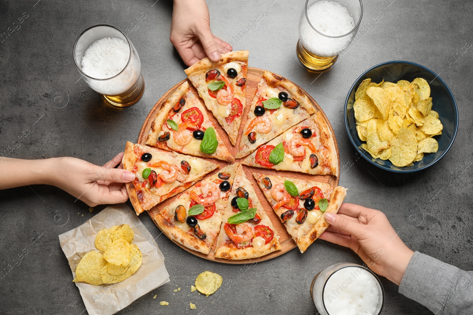 Photo of People taking slices of tasty pizza with seafood at grey table, top view