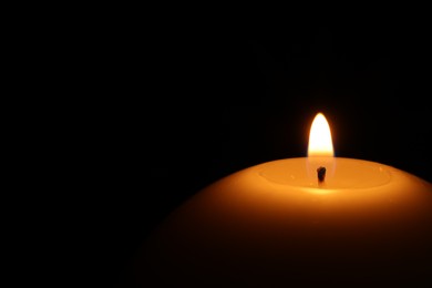 Photo of Burning wax candle on black background, closeup. Space for text