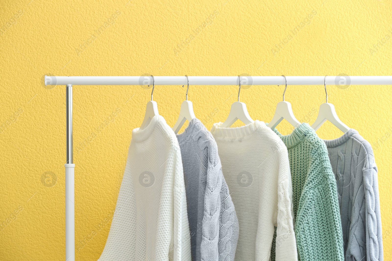 Photo of Collection of warm sweaters hanging on rack near yellow wall