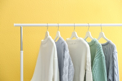 Photo of Collection of warm sweaters hanging on rack near yellow wall