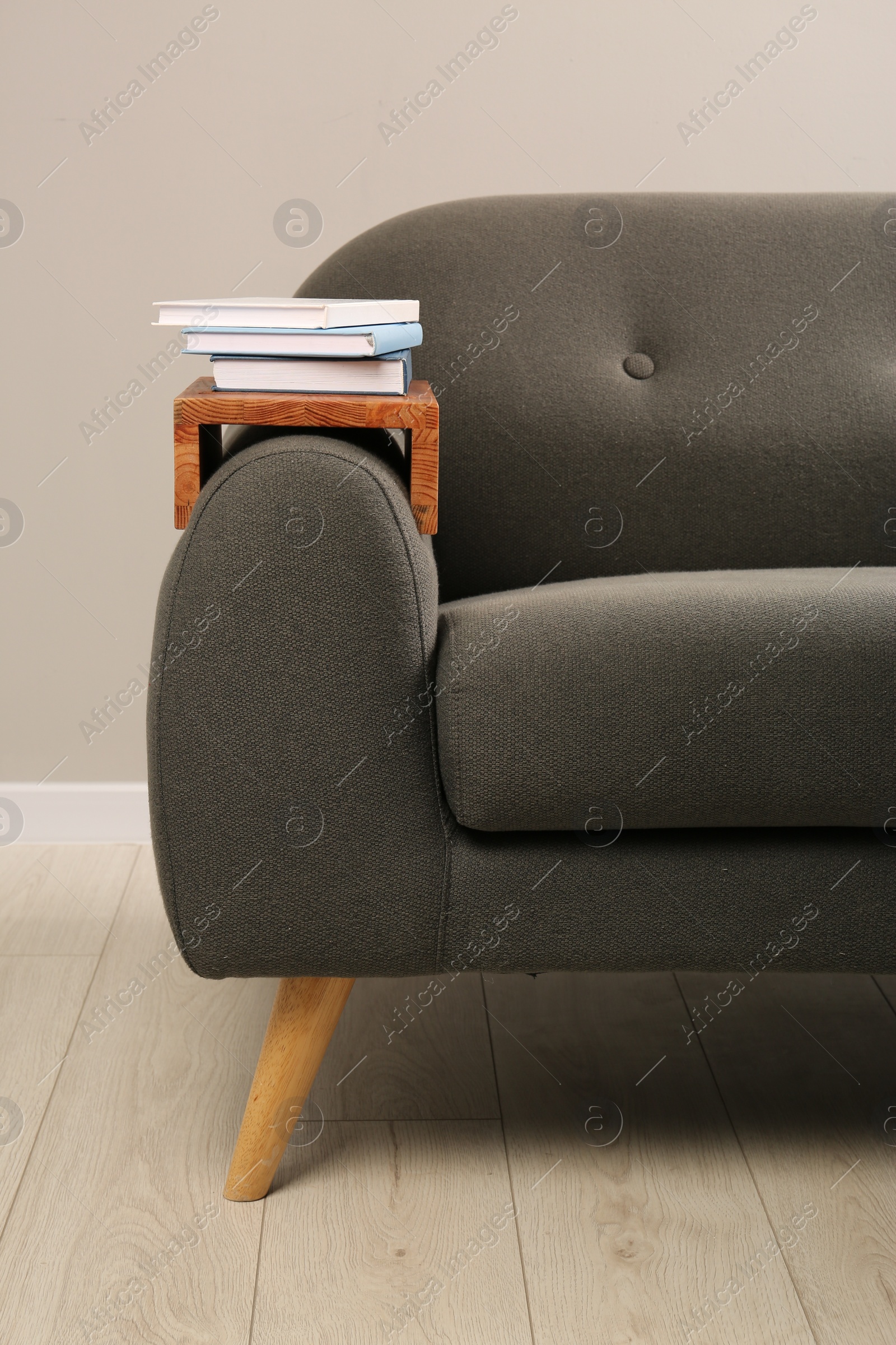 Photo of Books on sofa with wooden armrest table in room. Interior element