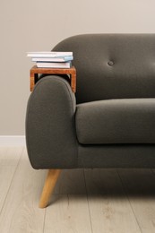 Books on sofa with wooden armrest table in room. Interior element