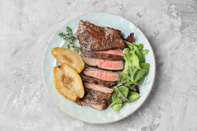 Pieces of delicious roasted beef meat, caramelized pear and greens on light textured table, top view