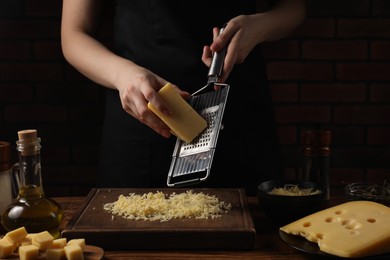 Photo of Woman grating cheese at wooden table, closeup