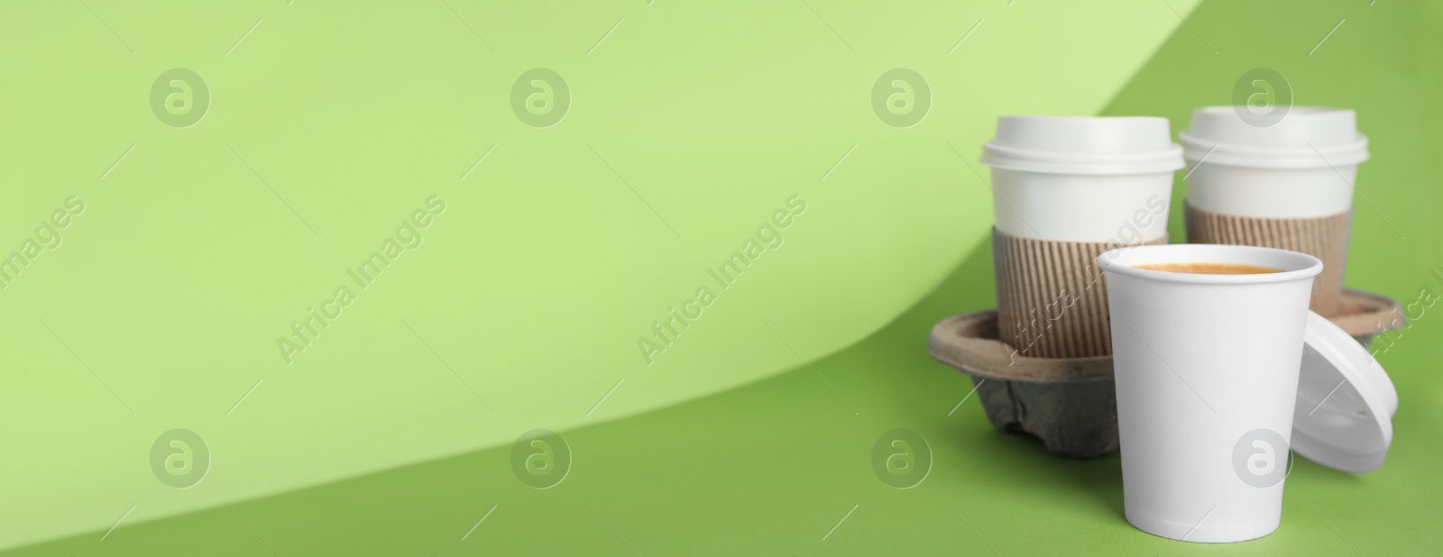 Image of Takeaway paper coffee cups with sleeves, plastic lids and cardboard holder on green background, space for text. Banner design