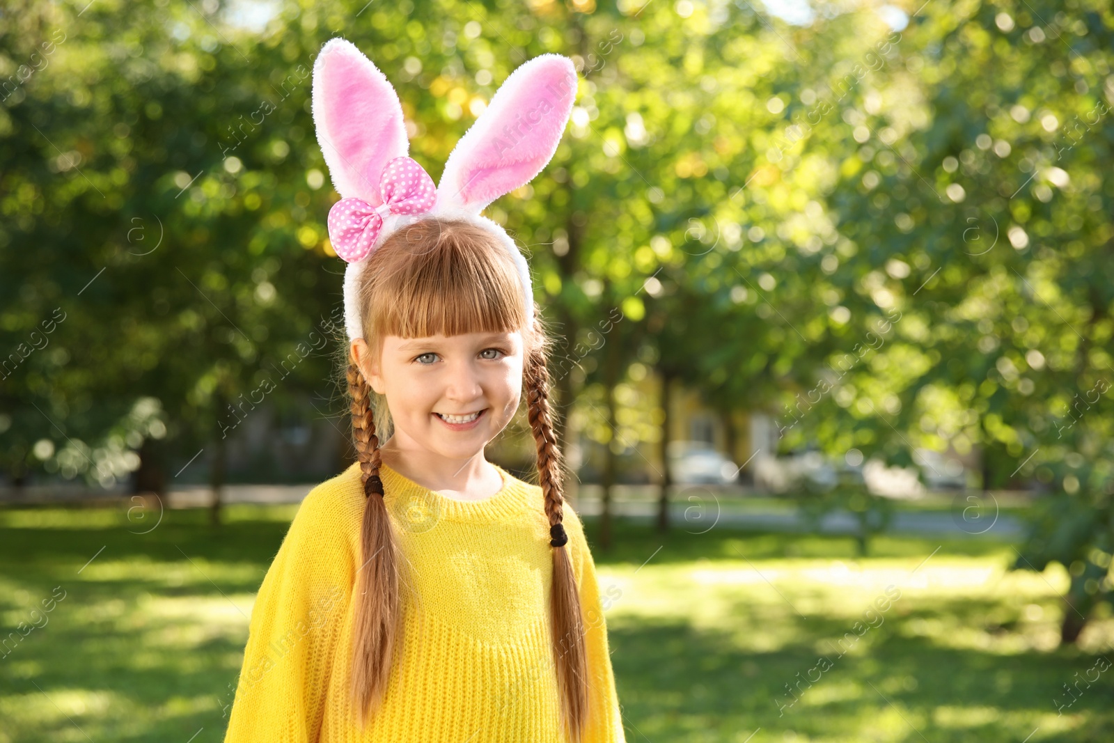 Photo of Cute little girl with bunny ears in park, space for text. Easter celebration