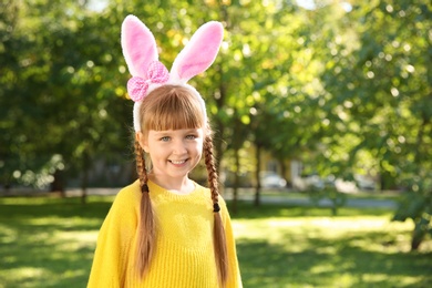 Photo of Cute little girl with bunny ears in park, space for text. Easter celebration
