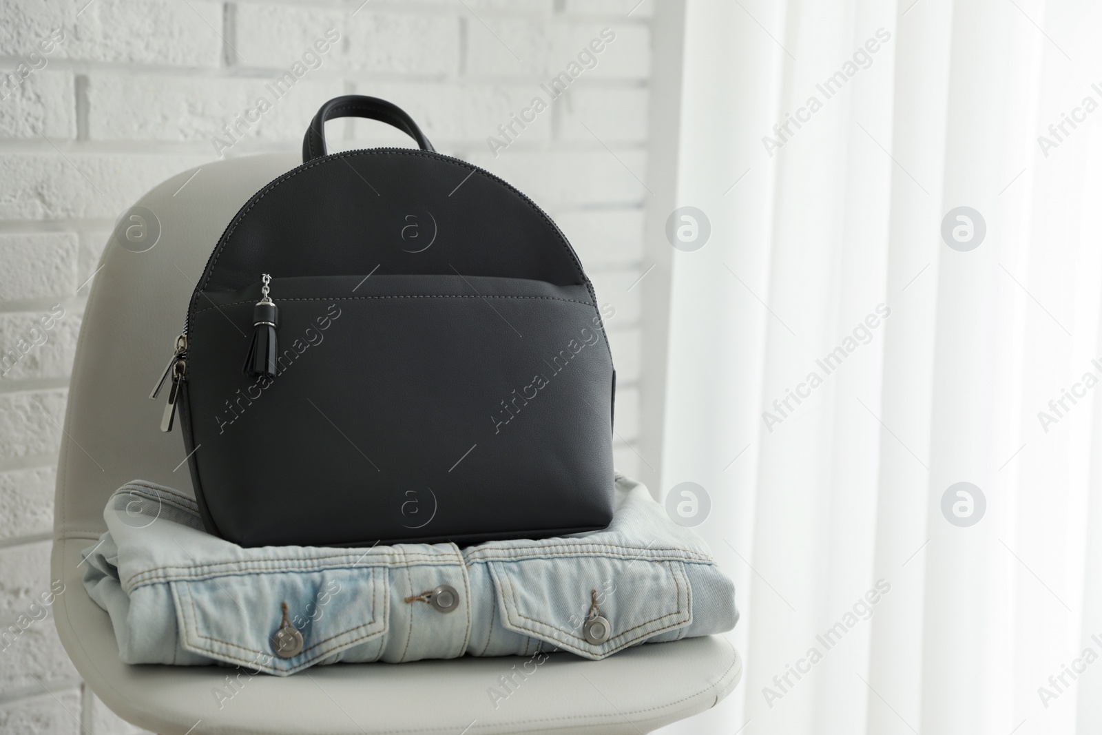 Photo of Stylish urban backpack and jacket on chair indoors. Space for text