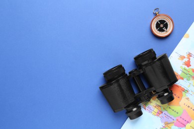 Photo of Modern binoculars, compass and world map on blue background, flat lay. space for text