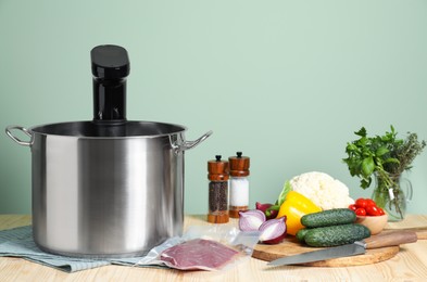 Photo of Meat in vacuum packing and other ingredients near pot with sous vide cooker on wooden table. Thermal immersion circulator