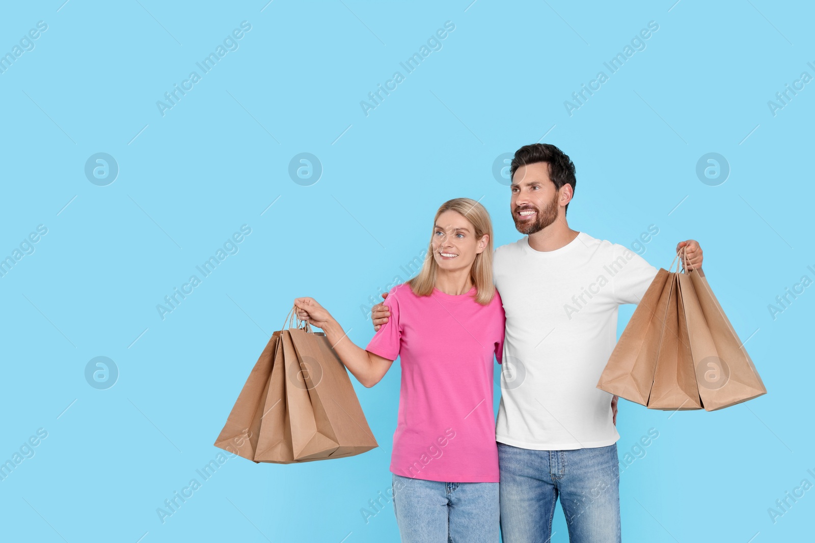 Photo of Family shopping. Happy couple with many paper bags on light blue background. Space for text