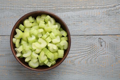 Photo of Fresh cut celery stalks in bowl on grey wooden table, top view. Space for text
