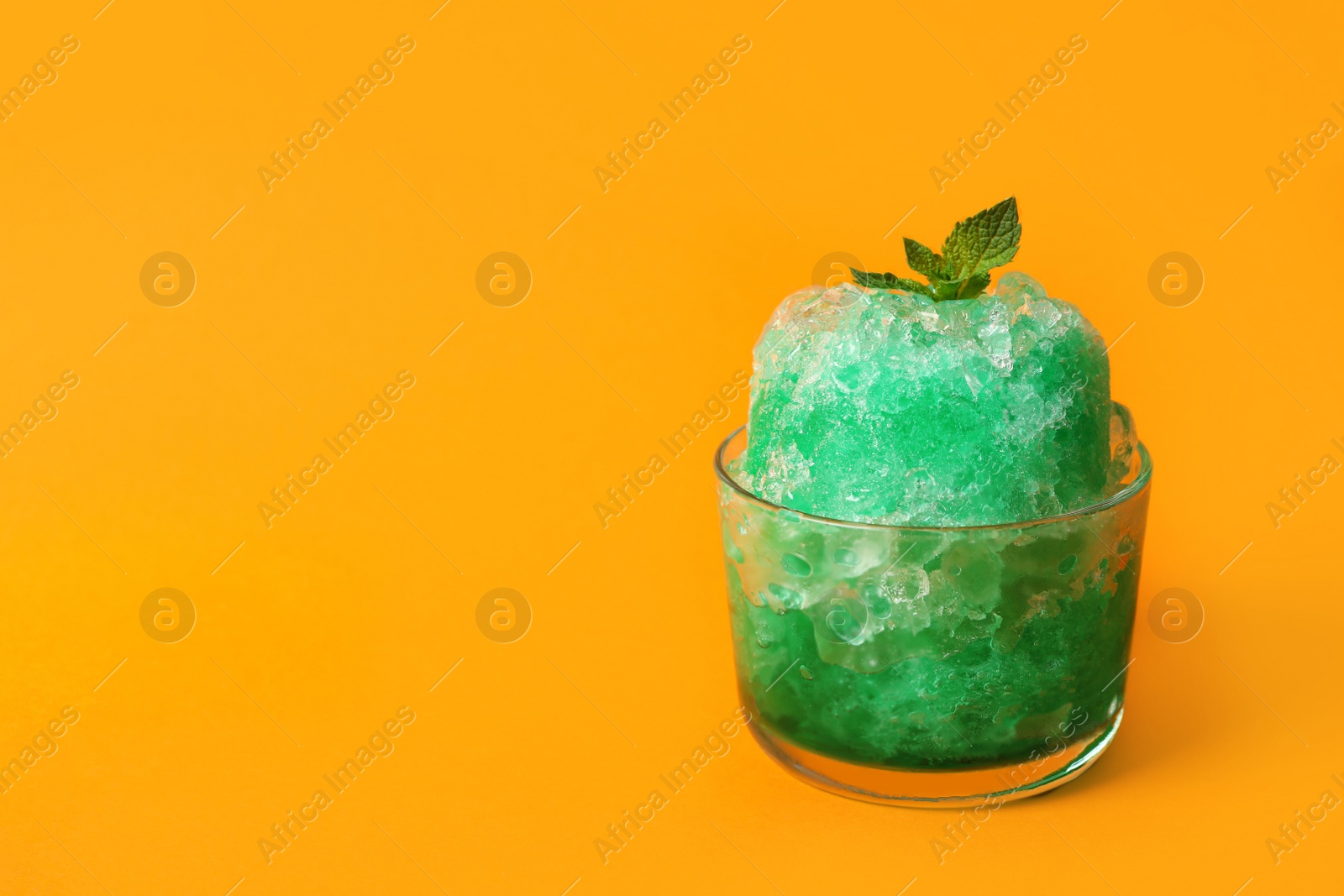 Photo of Shaving ice in glass dessert bowl on orange background, space for text