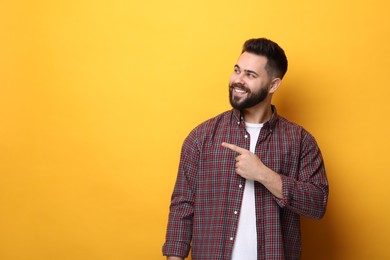 Photo of Happy young man with mustache pointing at something on yellow background. Space for text