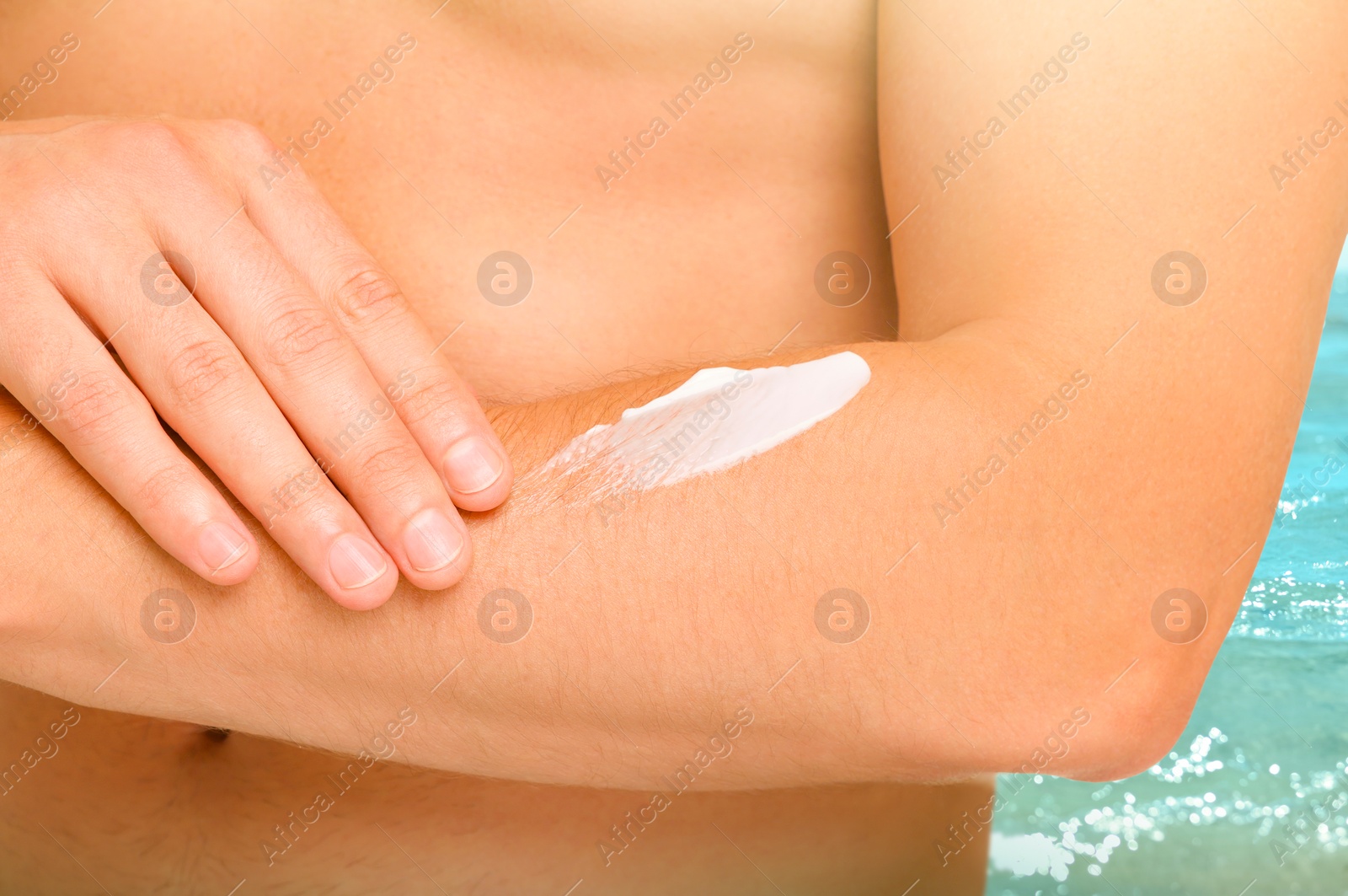 Image of Sun protection. Man applying sunblock onto skin near sea, closeup