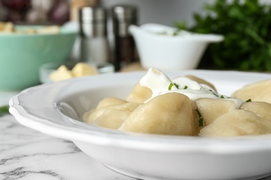 Photo of Delicious cooked dumplings with sour cream on white marble table, closeup