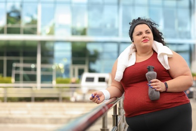 Photo of Beautiful overweight woman in sportswear with bottle and towel outdoors