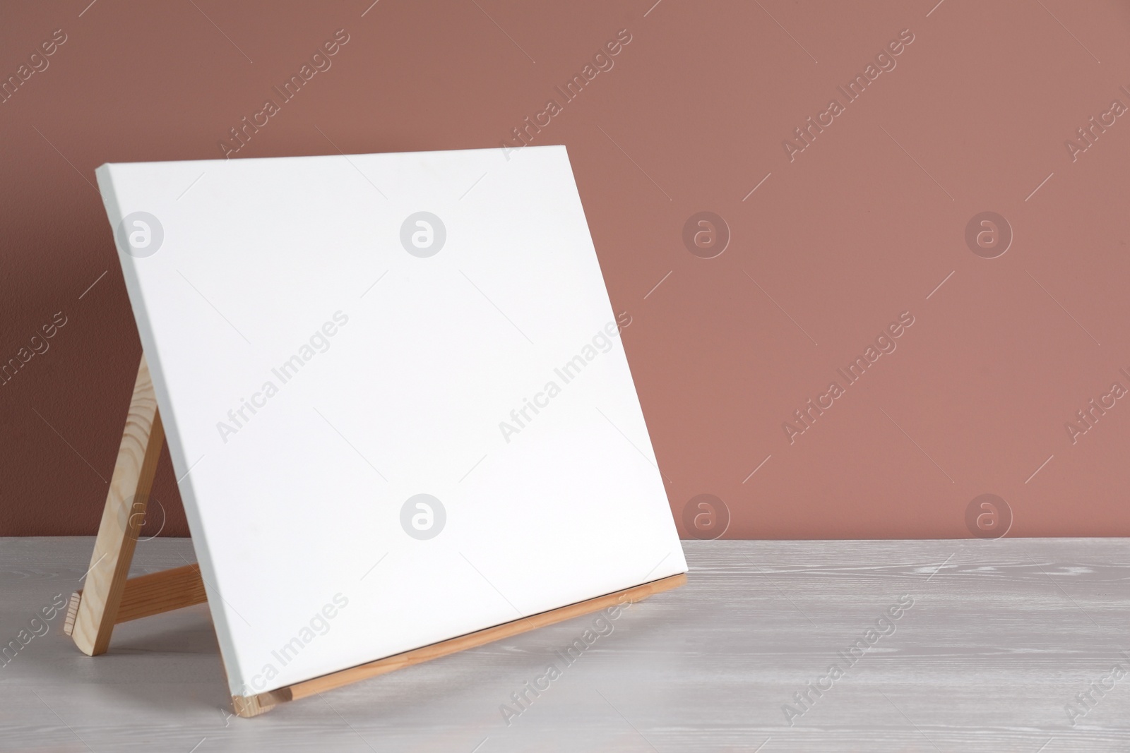 Photo of Wooden easel with blank canvas on white table. Space for text