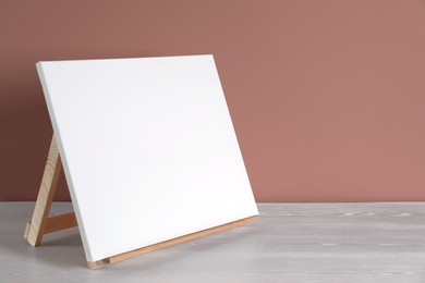 Wooden easel with blank canvas on white table. Space for text